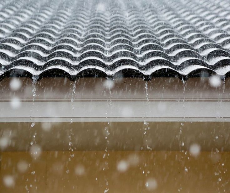 Rain running off a corrugated roof edge into the gutter line during a Denver storm